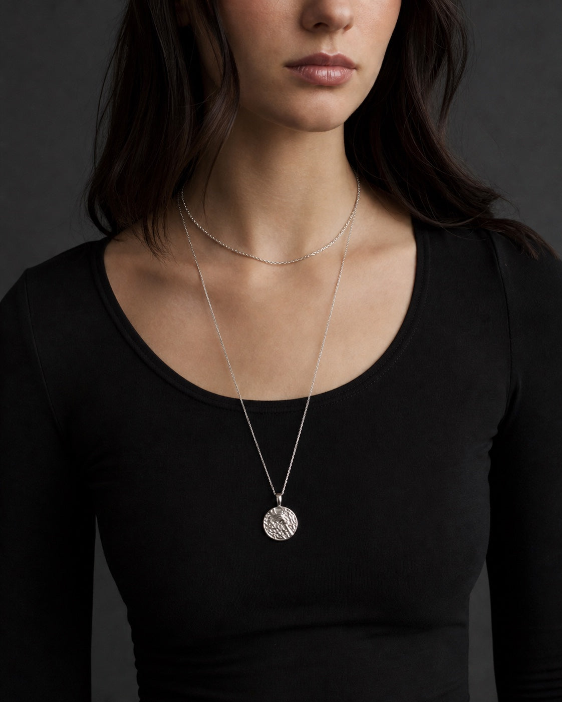 Model wearing layered silver pendant necklaces